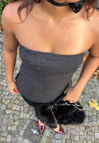 Grey strapless top, fitted design; black trousers; shiny red pointed heels; small black faux fur handbag with a chain strap. Cobblestone background.