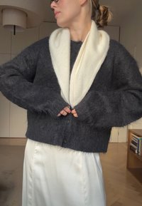 Grå, blød cardigan med overdådig kappehals i creme, med lange ærmer og knaplukning, kombineret med en cremefarvet satin nederdel.