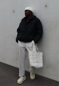 Giacca a vento nera, berretto in maglia bianco, pantaloni beige chiaro, borsa a mano crema e zoccoli bianchi con fori. Superfici testurizzate e design a strati.