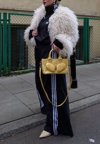 Black athletic tracksuit featuring white stripes, a fluffy white faux fur coat, a yellow handbag with two front pockets, and beige pointed-toe heels.