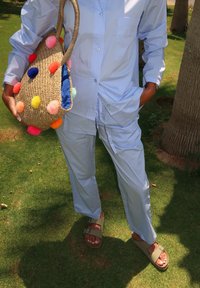 Ανοιχτό μπλε, φαρδύ πουκάμισο και παντελόνι από ύφασμα. Ύφαντη τσάντα με πολύχρωμες φουντίτσες. Ελιές πράσινα σανδάλια με πόρπες.