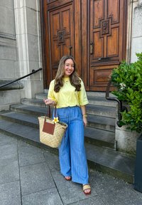Yellow t-shirt, blue striped wide-leg trousers, woven straw bag with brown accents and floral detail, and brown slide sandals.
