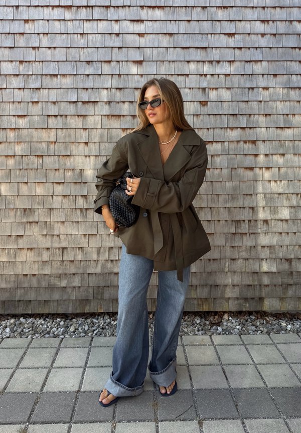 Olivenfarvet oversized blazer med brede revers, knyttet talje, sammen med løse lyseblå jeans og en sort vævet clutch. Moderne solbriller fuldender looket.