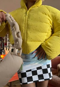 Doudoune jaune avec accents en strass, manches surdimensionnées, associée à une jupe bleu clair ornée de nuages et d'un ourlet à carreaux noirs et blancs.