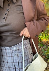 Polo marron côtelé avec boutons et logo, associé à un blazer marron et une jupe à carreaux avec boucles argentées. Accessoire : sac à main blanc tissé.