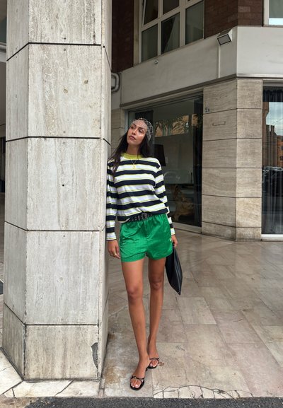 Camisa de manga larga a rayas en negro y amarillo, combinada con pantalones cortos verdes. El conjunto incluye un cinturón ancho, un bolso negro y sandalias con tiras.