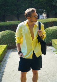 Kollane linane särk, krae avatud, mustade lühikeste pükstega. Aksessuaarideks on must kott ja käevõrud. Rohelised päikeseprillid lõpetavad välimuse.