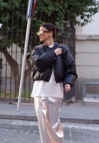 Μαύρο κοντό φουσκωτό μπουφάν, άσπρο μπλουζάκι από κάτω και μεταλλική ασημένια μακριά φούστα. Τα αξεσουάρ περιλαμβάνουν oversized γυαλιά και δαχτυλίδια.