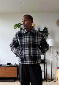 Veste zippée à carreaux noirs et gris en polaire douce, dotée d'un col, de deux poches latérales et d'une coupe légèrement raccourcie.