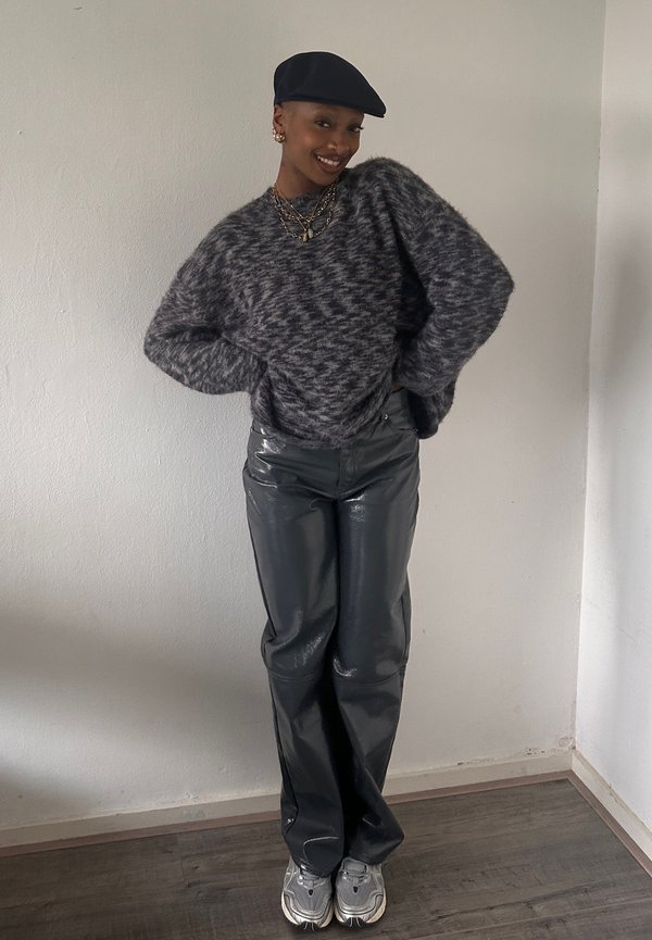 Suéter gris y negro con patrones, pantalones negros brillantes de cintura alta y zapatillas gris claro, todo contra un fondo neutro.