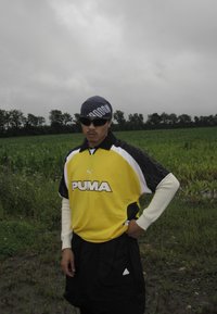 Yellow and black Puma sports jersey with short sleeves, teamed with black shorts. A blue bandana, sunglasses, and a field in the background.