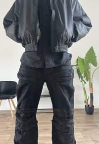 Czarna kurtka bomberka z elastycznymi mankietami i pasem, noszona na czarnej koszuli zapinanej na guziki. Czarny, przetarty denim z rozdarciami na kolanach.