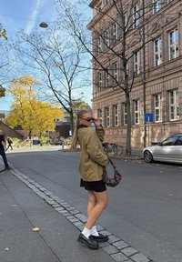 Oljčno zelena jakna, črna mini krilo, bele nogavice, črni platformni čevlji, rjava torbica. Mesto ulica z drevesi in jesenskim listjem.