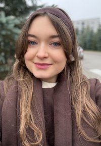 Bruine sjaal en trui, gestructureerde stof, off-white kraag, lang bruin haar, natuurlijke make-up, buitenomgeving met wazige groene achtergrond.