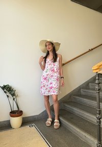 Φλοράλ αμάνικο φόρεμα σε λευκό χρώμα με ροζ και πράσινα μοτίβα. Καπέλο από ψάθα με φαρδύ γείσο, μπεζ σανδάλια και γλάστρο με πράσινο φυτό κοντά.