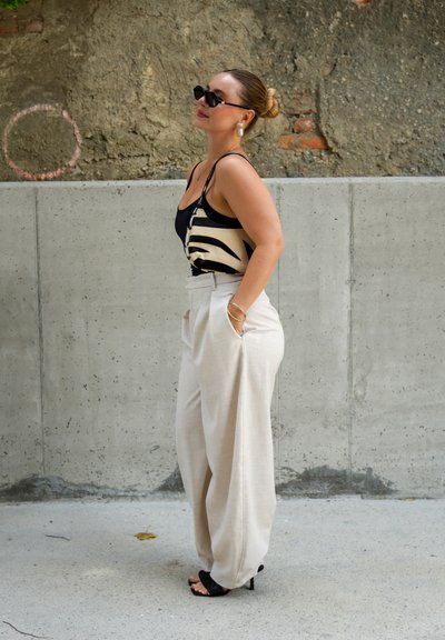 Top de tirantes negro y beige a rayas, combinado con pantalones de pierna ancha beige claros. Sandalias de tacón negras, accesorios mínimos.