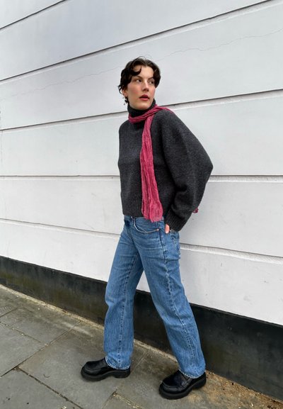 Suéter gris texturizado con cuello alto, combinado con jeans de mezclilla azules y botas de plataforma negras. Una bufanda rosa cae alrededor del cuello.