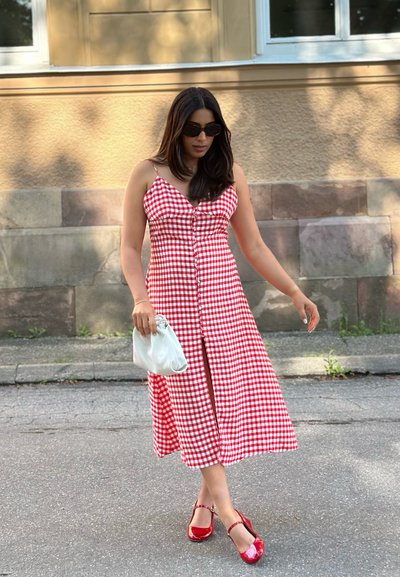 Vestido midi de cuadros vichy rojos y blancos con botones en la parte delantera, diseño de abertura, combinado con tacones rojos y un bolso de mano blanco.