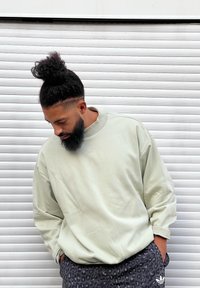 Sweatshirt verde claro, de tamanho grande, feita de material macio com gola alta e logo subtil. Combinada com calções cinzentos com estampa de leopardo.