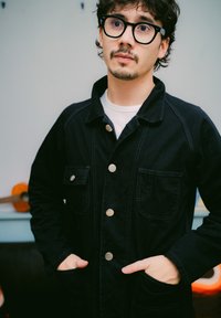 Svart denimjakke med sølvknapper, to brystlommer og kontrastsøm. Stoffet har en glatt tekstur og en avslappet passform.