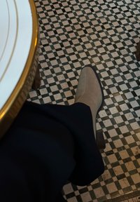 beezid nubukist kottid kitsa ninaga ja ploki kontsaga, asetatud must-valge ruudulisele plaatpõrandale, osaliselt varjatud tumedate pükstega.