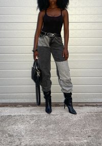 Body nero, pantaloni in denim a blocchi di colore neri e grigi, stivali neri con tacco alto e borsa nera con strap per spalla.