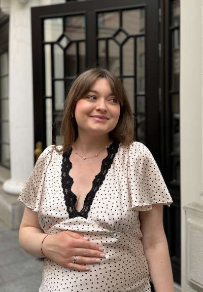 Blusa rosa claro con lunares negros, escote de encaje, mangas acampanadas y cintura fruncida. Situada frente a una puerta enmarcada en negro.