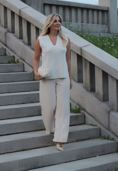 Top sin mangas de color crema con escote en forma de V y textura acanalada, combinado con pantalones de pierna ancha. Accesorios de un suave bolso de mano con recogidos.