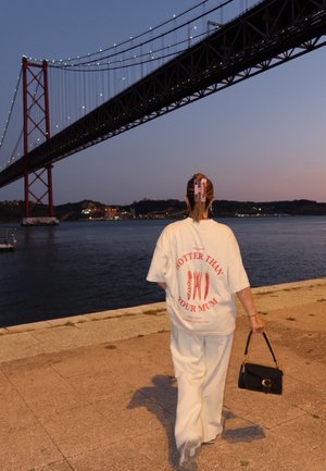 Camiseta blanca de gran tamaño con texto y gráficos en rojo; combinada con pantalones blancos holgados. El accesorio incluye un bolso negro y pinzas para el cabello.