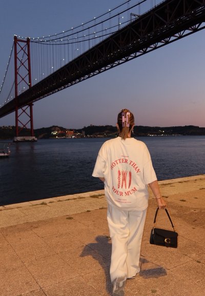 Camiseta blanca de gran tamaño con texto y gráficos en rojo; combinada con pantalones blancos holgados. El accesorio incluye un bolso negro y pinzas para el cabello.