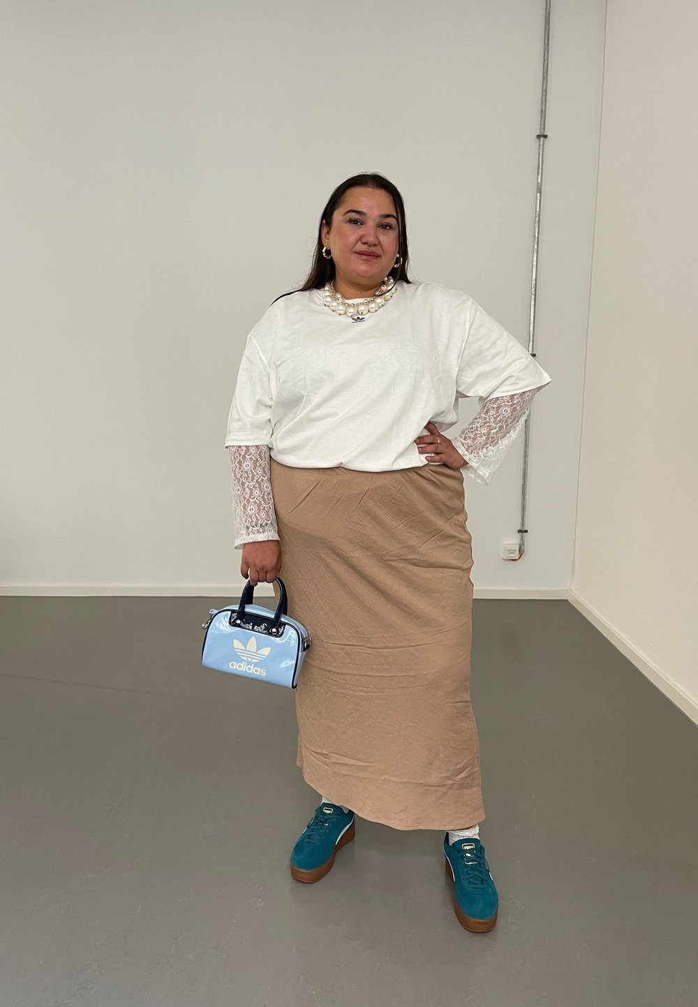 Λευκό μπλουζάκι με δαντελένια μανίκια, μπεζ φούστα, ανοιχτό μπλε τσάντα, τιρκουάζ παπούτσια με καφέ σόλες. Μαργαριταρένιο κολιέ ως αξιοσημείωτο αξεσουάρ.