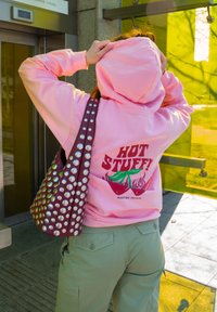 Rosa hettegenser med "HOT STUFF!" grafikk, grønne detaljer og flammer. Olivengrønne cargo-bukser og en bordeaux ryggsekk med metallstifter. Utendørs t-banestasjon inngang.