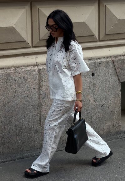 Conjunto de top y pantalones de algodón blanco bordado con recortes florales, sandalias de plataforma negras y un bolso negro con herrajes dorados.
