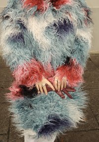 Texturált, többszínű, kék, piros és fehér árnyalatú bolyhos kabát, hosszú szálas anyagból. Kéz barna borítéktáskát tart.