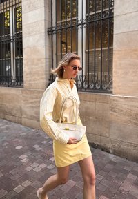 Witte handtas met korte handvaten, gele accenten, gecombineerd met een gele rok en gestreepte, oversized blouse met lange mouwen in pasteltinten.