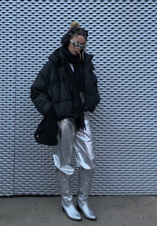 Chaqueta de plumas negra, blusa blanca, pantalones plateados brillantes, botas de cowboy plateadas y bufanda negra. Los accesorios incluyen auriculares y gafas de sol únicas.
