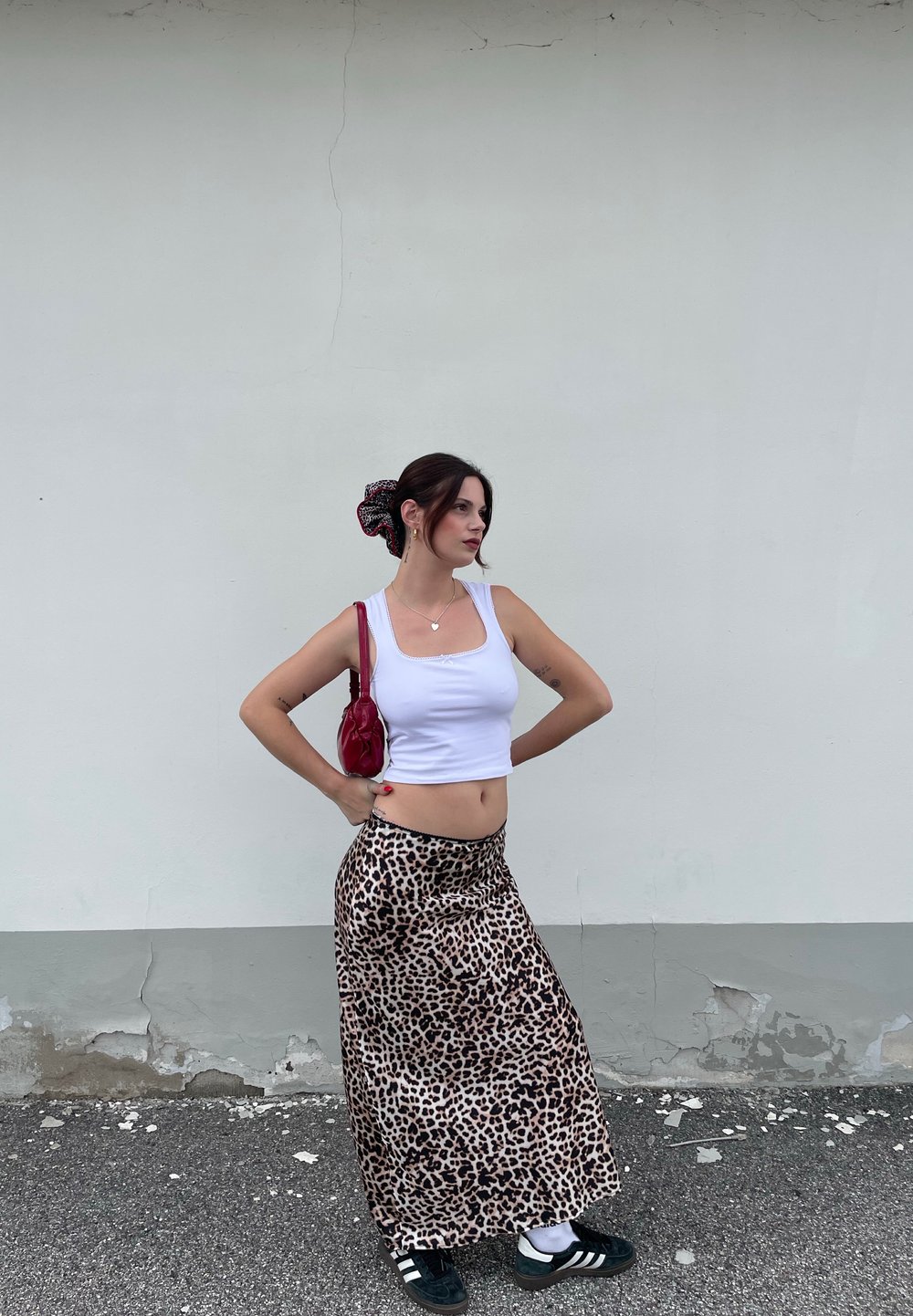 Weißes, kurzes Tanktop, Maxiröcke mit Tiermotiv in Beige und Braun, schwarze Sneakers, rote Handtasche, schwarze und rote Haargummis, glatte Textur.