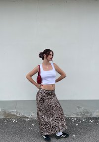 Weißes, kurzes Tanktop, Maxiröcke mit Tiermotiv in Beige und Braun, schwarze Sneakers, rote Handtasche, schwarze und rote Haargummis, glatte Textur.