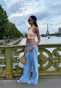 Top a maniche corte beige, jeans a gamba larga azzurri, sneakers bianco e nero, con una borsa beige e la Torre Eiffel sullo sfondo.