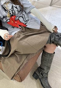 Raitatavallinen napillinen paita, jossa on sarjakuvakani aihe, beigelöydä, ja harmaat polven yli yltävät saappaat, joissa on solk yksityiskohta. Musta käsilaukku lyhyellä kahvalla.