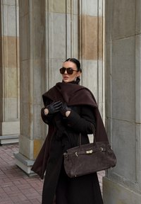 Tumšs vilnas mētelis ar jostu, pārlikts ar brūnu apmetni. Melnas cimdi un pārmērīgi lieli saulesbrilles. Brūna zāģētas zamšādas soma ar zelta aparatūru.