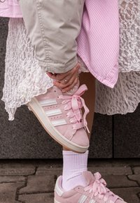 Roze suède sneakers met witte accenten en dikke roze veters. Draag ze met witte kant en gestreepte stoflagen, die textuurdetails tonen.