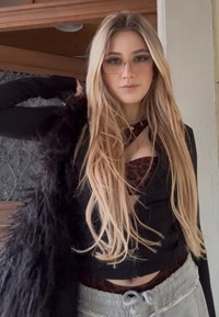 Jeune femme aux longs cheveux blonds portant des lunettes, une veste noire par-dessus un haut imprimé léopard et un pantalon de survêtement gris à l'intérieur.