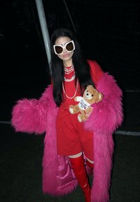 Pink faux fur coat, red dress and glossy red over-the-knee boots. Accessories include oversized white sunglasses and a stuffed bear.