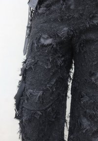 Černé kalhoty s texturovaným povrchem, které mají třepený design látky, kombinující detailní vzory a hladký černý pas.