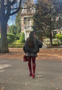 Υπερυψωμένο σκούρο γκρι φούτερ, πλισέ γκρι φούστα, μπορντώ καλσόν και γυαλιστερά μπορντώ μπότες μέχρι το γόνατο. Κρατώντας μια υφασμένη μπορντώ τσάντα.