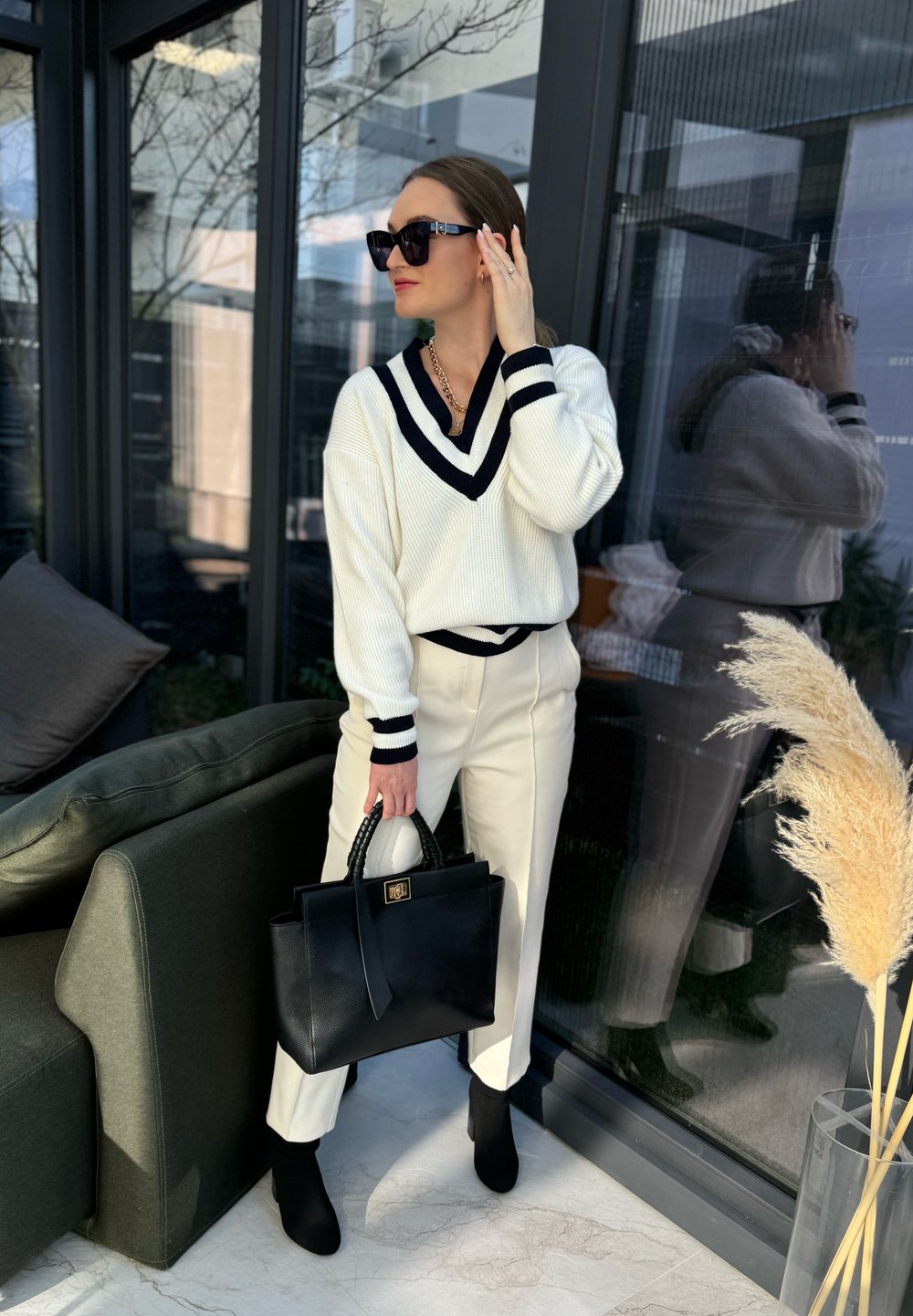 Λευκό ριμπ μπλούζα με navy ρίγες, κρέμα παντελόνι και μαύρη τσάντα χειρός. Μαύρες μπούτες μέχρι τον αστράγαλο, γυαλιά ηλίου και περιστασιακά κολιέ ολοκληρώνουν την εμφάνιση.