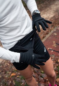 Fekete futóshort cipzáras zsebbel, fekete kesztyűkkel és fehér hosszú ujjú inggel párosítva. A szövet rugalmas és testhez simuló.