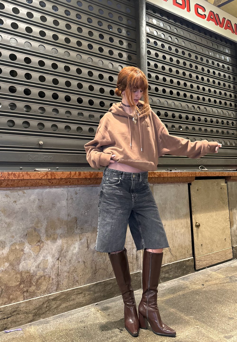 Brauner Kapuzenpullover, graue Jeansshorts und braune kniehohe Stiefel mit Absatz. Glattes Material, lockere Passform und leichte Used-Optik bei den Shorts.