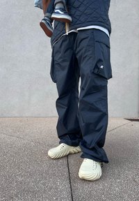 Navy waterproof cargo trousers featuring multiple pockets, paired with cream-coloured textured slip-on shoes. Casual fit and functional design.